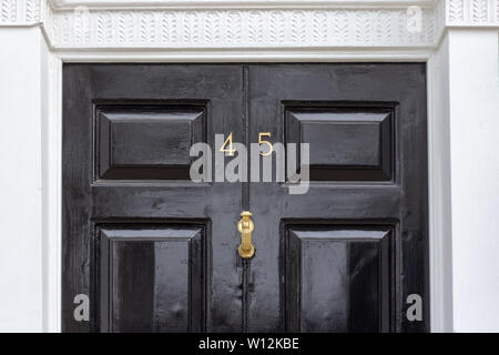 Haus Nummer 45 mit den vierzig - fünf in Metall Ziffern auf einem schwarz lackierten alte hölzerne Eingangstür mit geschnitzten weißen Stein Türrahmen Stockfoto