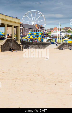 Der Sandstrand und Riesenrad auf Barry Island sind hell erleuchtet durch Sonnenschein und sich gegen die dunklen Wolken im Himmel auf einem frühen Sommer Tag Stockfoto