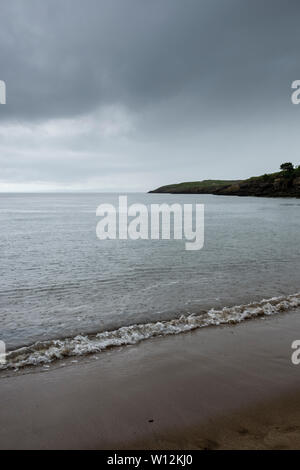 Das Meer, Pocked durch Regen gekennzeichnet während eines schweren Dusche, ist ruhig und runden Sie vorsichtig an den Strand. Im Hintergrund ist ein dunkler Landspitze unter einem stürmischen Himmel. Stockfoto