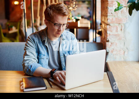 Junger Mann in Jeans shirt Arbeiten am Laptop im Cafe. Stockfoto