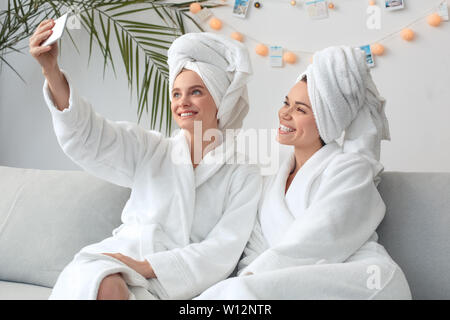 Junge Frauen Rest zusammen zu Hause Beauty Care sitzen auf einem Sofa tragen Handtücher nehmen selfie Fotos auf dem Smartphone lächelt fröhlich Seitenansicht Stockfoto