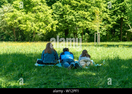 Drei Personen in einem Park, die auf dem Gras. Sie sind von hinten gezeigt. Eine Frau und Mann liegen und auf Frau sitzt. Stockfoto