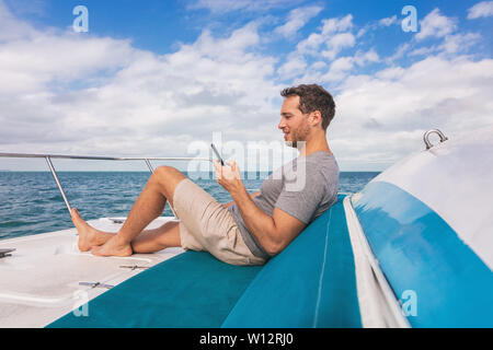 Boot Mann mit Handy Textnachrichten auf Sat-Internet und entspannen Sie an Deck der Yacht Luxus Lifestyle. Stockfoto