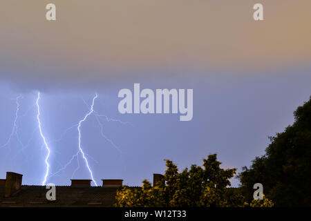 Blitzeinschläge hinter Gebäude bei Unwetter in Kroatien. Blitzschlag aus grauen Gewitterwolken. Stockfoto
