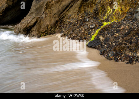 Wellen gegen Steine, Moos und eine Höhle in Laguna Beach, Kalifornien. Lange Belichtung Stockfoto