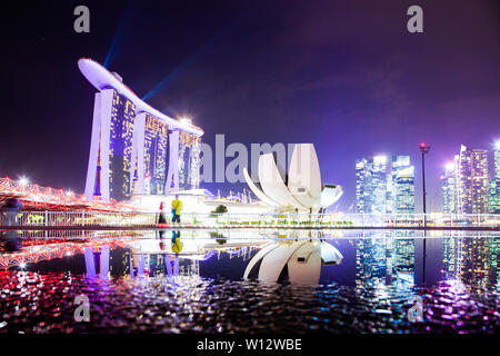 Singapur, Singapur - März 2019: Skyline von Singapur Marina Bay bei Nacht mit Marina Bay Sands und Kunst Science Museum in einem Teich spiegelt nach Ra Stockfoto