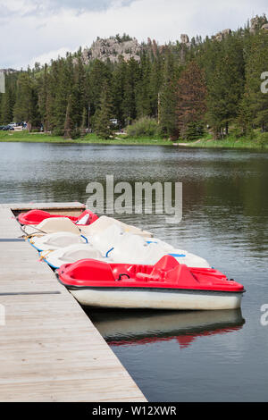 Rote und weiße Paddelboote in einer Reihe entlang einem Dock in Sylvan Lake in South Dakota mit einem weit entfernten Ufer von Bäumen, Fahrzeuge und Granit Berge. Stockfoto