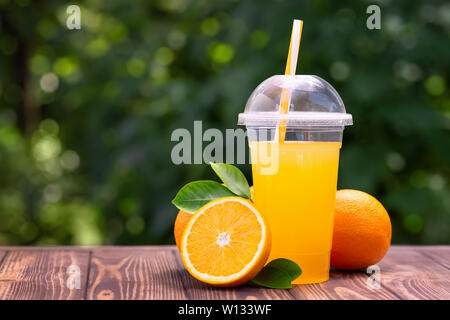Frisch gepresster Orangensaft in Schale aus Kunststoff auf Holz Tisch im Freien. Nehmen Sie Glas mit Sommer erfrischendes Getränk Stockfoto