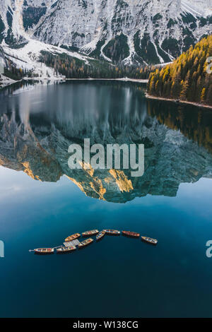 Herbst Landschaft des Lago di Pragser See in den italienischen Dolomiten in Norditalien. Drone Luftbild mit Booten aus Holz und schönen reflectio Stockfoto