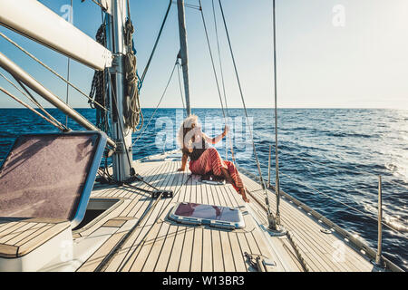 Die Menschen genießen reisen Abenteuer mit alternativer Transport weg - Schöne lockige blonde Frau, sitzen Sie auf einem Segelboot mit Meer und Himmel um-e Stockfoto