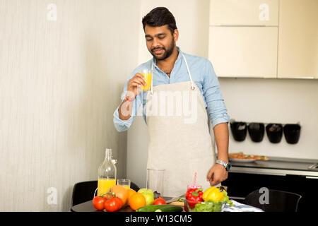 Hübscher junger angenehme bärtigen Inder trinken frisch gepressten O-Saft, Gemüse Smoothie, Zubereitung von Salat in der Küche. Gesunde f Stockfoto