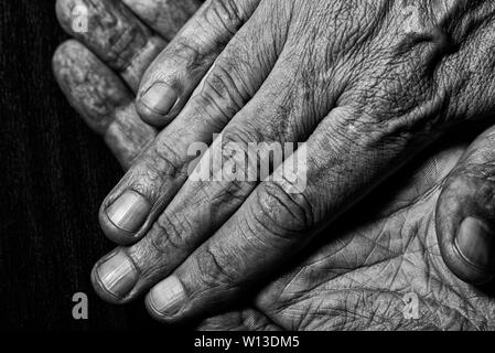 Schwarz-weiß Foto von älteren Mann gekreuzten Händen Detail auf dunklem Hintergrund Stockfoto
