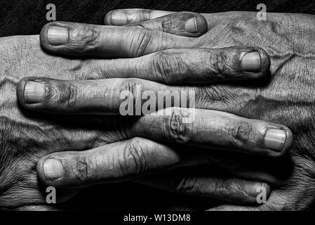 Schwarz-weiß Foto von älteren Menschen Hände mit gekreuzten Fingern auf dunklem Hintergrund Stockfoto
