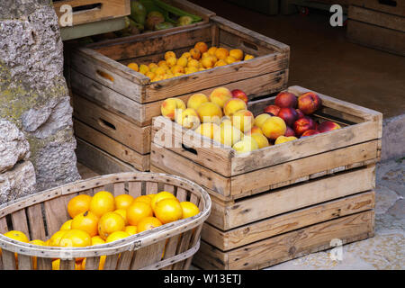 Reifen Orangen, Pfirsiche, Nektarinen, Pflaumen und Birnen in Holzkisten und einem Korb an einem Lebensmittelmarkt, eine Biene auf Orangen sitzen - abgewinkelten Seite anzeigen Stockfoto