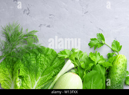 Hintergrund mit grünem Gemüse, Salat, Gurken, grüne Zwiebeln und Zucchini auf grauem Stein table top. Gesunde Ernährung Konzept mit kopieren. Stockfoto