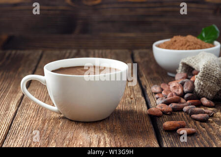 Kakao trinken in Weiß Becher, Kakaopulver und Kakaobohnen auf hölzernen Tisch. Stockfoto