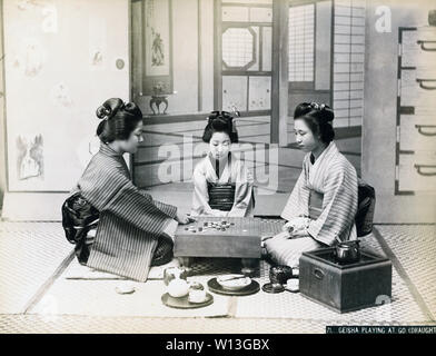 [1890s Japan - das Spiel von Go] - Zwei junge Frauen im Kimono und traditionellen Frisuren sind ein Spiel der gehen. Eine dritte Frau an schaut. Einen Topf Wasser eingehalten wird, heiß auf den hakohibachi, ein Aufsatz in einer Holzkiste verpackt. 19 Vintage albumen Foto. Stockfoto