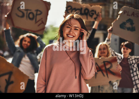 Speichern Sie Ihre Planeten. Junge Frau lächelnd und Gefühl glücklich während protestieren für Ökologie mit einer Gruppe von Aktivistinnen auf der Straße. Ökologie Konzept. Gruppe protestieren Stockfoto
