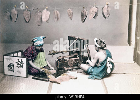[1870s Japan - Japanische Tabak Entscheidungsträger] - eine Frau und ein Mann in der traditionellen japanischen Kleidung werden die Tabakblätter. Der Mann ist mit einer Maschine. Die Frau ist das Bürsten lassen Sie eine mit einer kleinen Bürste. Einen kleinen Bildschirm können auf Ihrem linken gesehen werden. Im Hintergrund, Tabakblättern hängen aus einem String. 19 Vintage albumen Foto. Stockfoto
