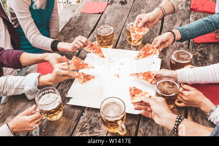 Gerne Freunde Essen nehmen Sie Pizza und Bier über einen alten Holztisch nach der Arbeit Stockfoto