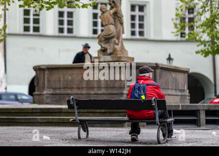 Prag, tschechische Republik - 12 April 2019: Ein einsamer alter Mann sitzt auf einer Bank vor einer Statue in der Mitte der Hauptstadt Prag Stockfoto