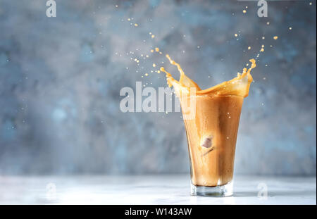 Splash in Glas Cappuccino auf blauem Hintergrund. Platz kopieren Stockfoto