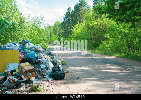 Illegale Deponie in der Nähe des Land sand Straße im Land an einem sonnigen Tag. Papierkorb Luftverschmutzung in der Natur. Dreckige Müllhalde in der Nähe der Wald Holz Stockfoto