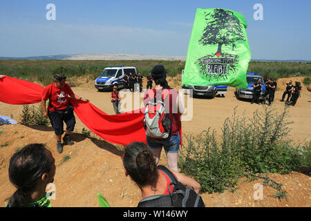 Kerpen, Deutschland. 30. Juni, 2019. Demonstranten Form ein Protest, eine so genannte Rote Linie, mit einer roten Fahne und einer "Hambacher Forst Bleibt' Flag zwischen dem Hambacher brown Coal Mine und des Hambacher Forst. Die Polizei im Hintergrund, so dass die Demonstranten nicht in Richtung der Grube verschieben. Quelle: David Young/dpa/Alamy leben Nachrichten Stockfoto