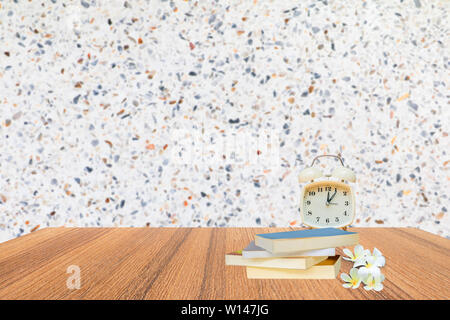 Wecker und Bücher auf Stein Regal Blumen plumeria in der Bibliothek der Schule Konzept mit Mauer blur Background Copy space Text hinzufügen Stockfoto