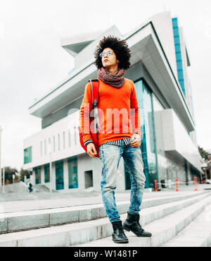 Eine junge afrikanische amerikanische Mann mit rotem backpackwalking in der Stadt. Stockfoto