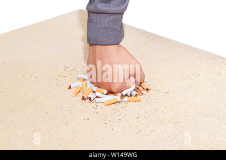 Männliche Hand zerquetscht Haufen Zigaretten ganz nah am Tisch terrazzo Bodenbelag gelb über weißen Hintergrund. health care Konzept, das Rauchen aufzugeben. Stockfoto