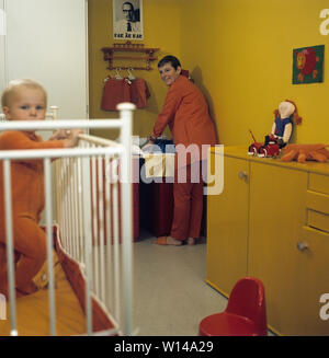 1960s Mutter. Eine junge Frau wird Reinigen und Wechseln von Windeln für ihr Baby, das auf einem wickeltisch liegt. Die Kleidung und Farben sind typisch 60er Jahre. Schweden 1964 Stockfoto