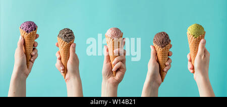 Hände halten Eis in der Waffel auf blauem Hintergrund. Eisportionierer in Kegel Sortiment in Frau Hände auf blauem Hintergrund. Banner Stockfoto