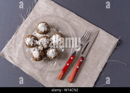 Gesunde bio Energie Kugeln mit Datteln, Backpflaumen, Rosinen, Erdnüsse, mit Kokos Späne, in eine Glasplatte auf grauem Hintergrund, flach. Stockfoto