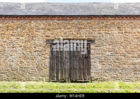 Watford, Northamptonshire, Großbritannien: Verfallene, verwitterte und teilweise verrottete doppelte Holztüren in der Wand einer Steinscheune mit Schieferdach. Stockfoto