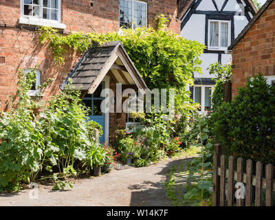 Eine altmodische Cottage in der Sonne mit einer Veranda, Dach und hübsche Blumen vor. Stockfoto