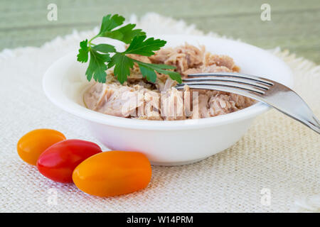 Thunfisch Filet in weißem Porzellan Schüssel, Gabel, Petersilie und drei Kirschtomaten auf eine beige Tabelle tabelle Serviette. Meeresfrüchte, gesundes Essen. Ansicht von vorn Stockfoto