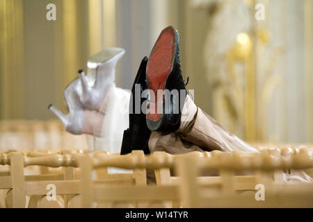 Ein Mann und eine Frau setzen ihre Füße auf dem Rücken der Stühle. Die Beine von einem Mann in Schwarz Schuhe und eine Frau in Silber Heels Stockfoto