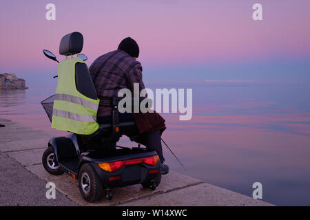 Person mit Hilfe eines persönlichen Mobilität scooter, ihm zu erlauben, die normale Tätigkeit zu tun eingeschränkter Mobilität. Ihn hier Angeln in den frühen Morgenstunden Stockfoto