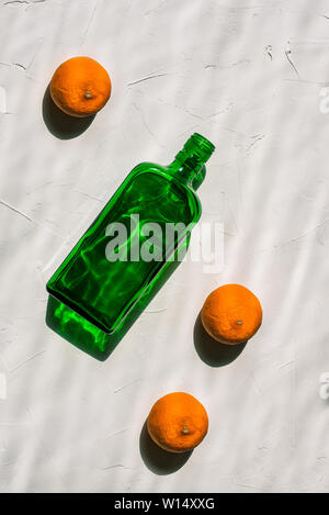 Grüne leere Flasche und drei Mandarinen auf einem weißen Hintergrund. Minimale noch leben. Helles Licht, harte Schatten und eine Reflexion aus der Flasche. Creativ Stockfoto