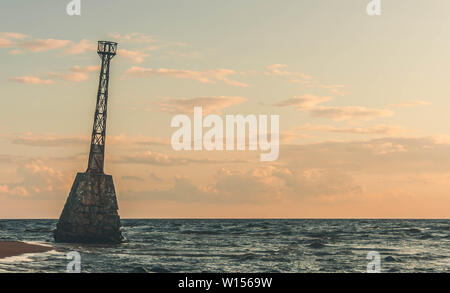 Alte, geneigt Beacon, stehend auf einem Ostseeküste während des Sonnenuntergangs. Vidzeme felsigen Küste in Lettland. Stockfoto