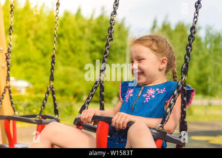 Glückliche kleine Mädchen spielen, bis ad unten gehen auf einer Wippe auf einem grasbewachsenen Spielplatz in unberührter Natur unter Bäumen. Gesunde Kindheit Konzept. Stockfoto