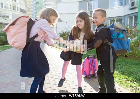 Outdoor Portrait von lächelnden Schulkinder in der Grundschule. Sind eine Gruppe von Kindern mit Rucksäcken Spaß haben, zu sprechen. Bildung, Freundschaft, technolo Stockfoto