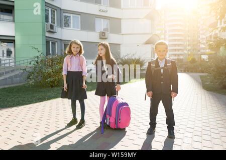 Outdoor Portrait von lächelnden Schulkinder in der Grundschule. Sind eine Gruppe von Kindern mit Rucksäcken Spaß haben, zu sprechen. Bildung, Freundschaft, technolo Stockfoto