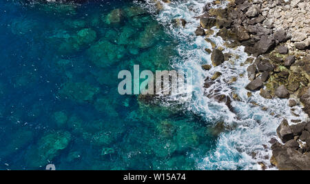 Antenne Blick von oben auf die kristallklare Wellen schlagen felsigen Strand erstellen weißer Schaum. Stockfoto