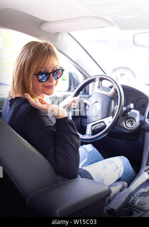 Frau in dem Auto innen hält Rad drehen um lächelnd mit Blick auf die Fahrgäste im Fond Stockfoto