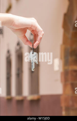 Ein paar Schlüssel für die Wohnung in der Hand eines Mannes auf dem Hintergrund einer braunen Haus mit Fenstern, die von der Tür in Form eines Bogens. Das Konzept Stockfoto