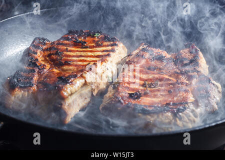 Rauch und Dampf Aufstieg aus einem Schwein Steak auf dem Grill Pfanne Stockfoto