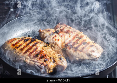 Rauch und Dampf Aufstieg aus einem Schwein Steak auf dem Grill Pfanne Stockfoto
