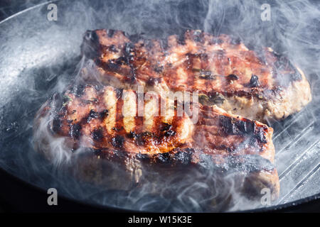 Rauch und Dampf Aufstieg aus einem Schwein Steak auf dem Grill Pfanne Stockfoto
